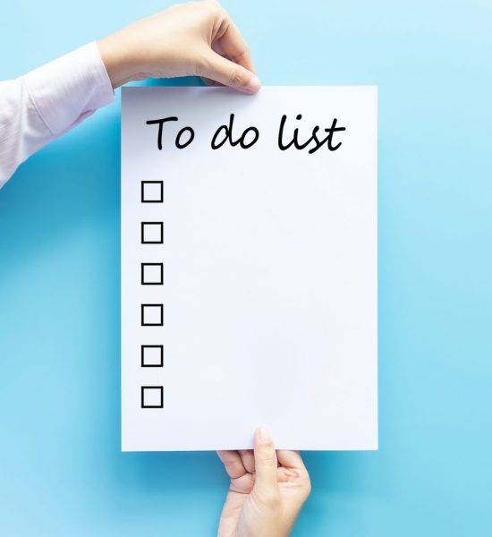 Photo of a Caucasian individual's hands holding a large white piece of paper with the words "To-Do List" at the top. On the left side of the paper is a column of boxes to be checked off after completing tasks.
